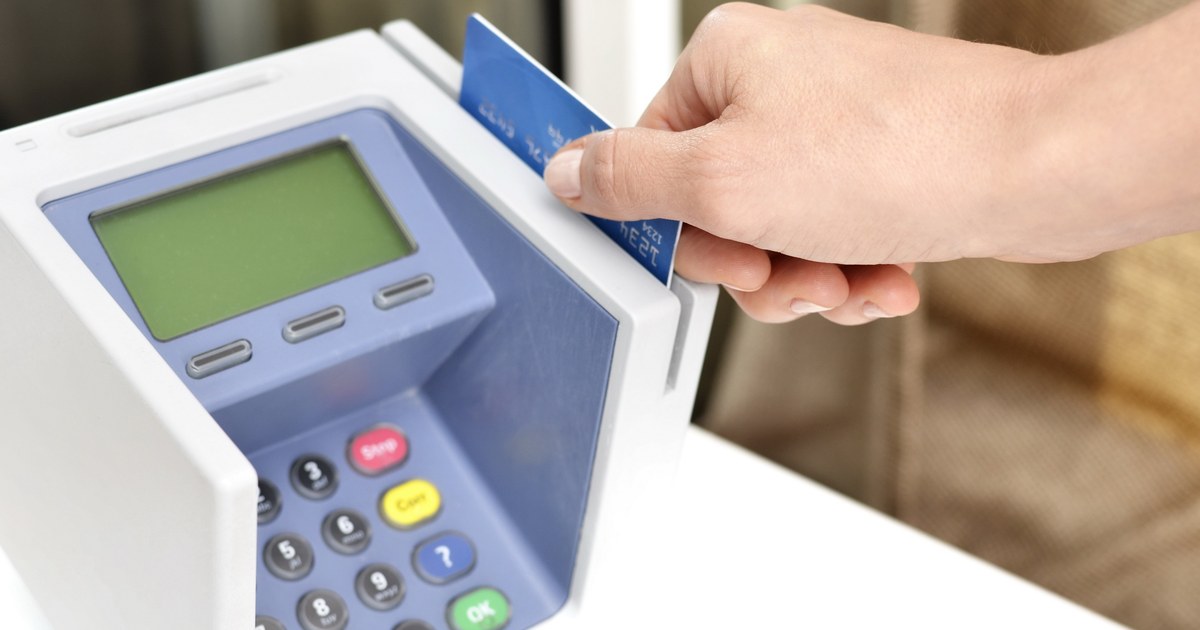 A hand inserting a brand-neutral payment card into a card terminal, illustrating banking and payment controls.