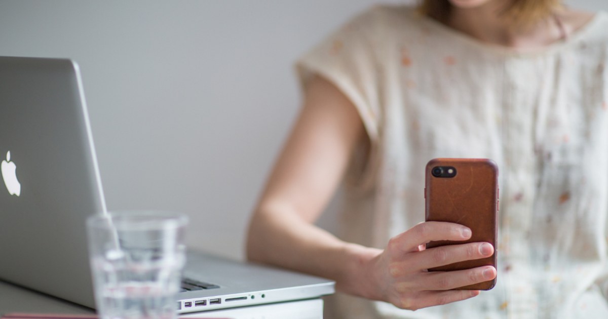 Person using a smartphone and laptop at a desk to manage online payments