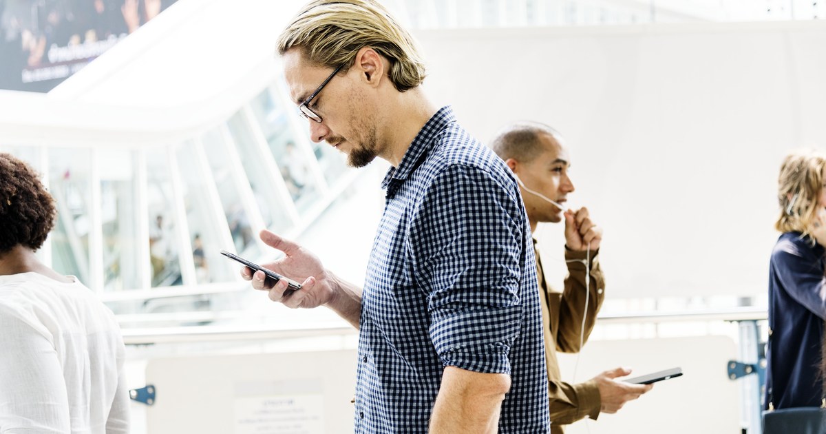 A person concentrating on a smartphone screen while standing in a bright public space