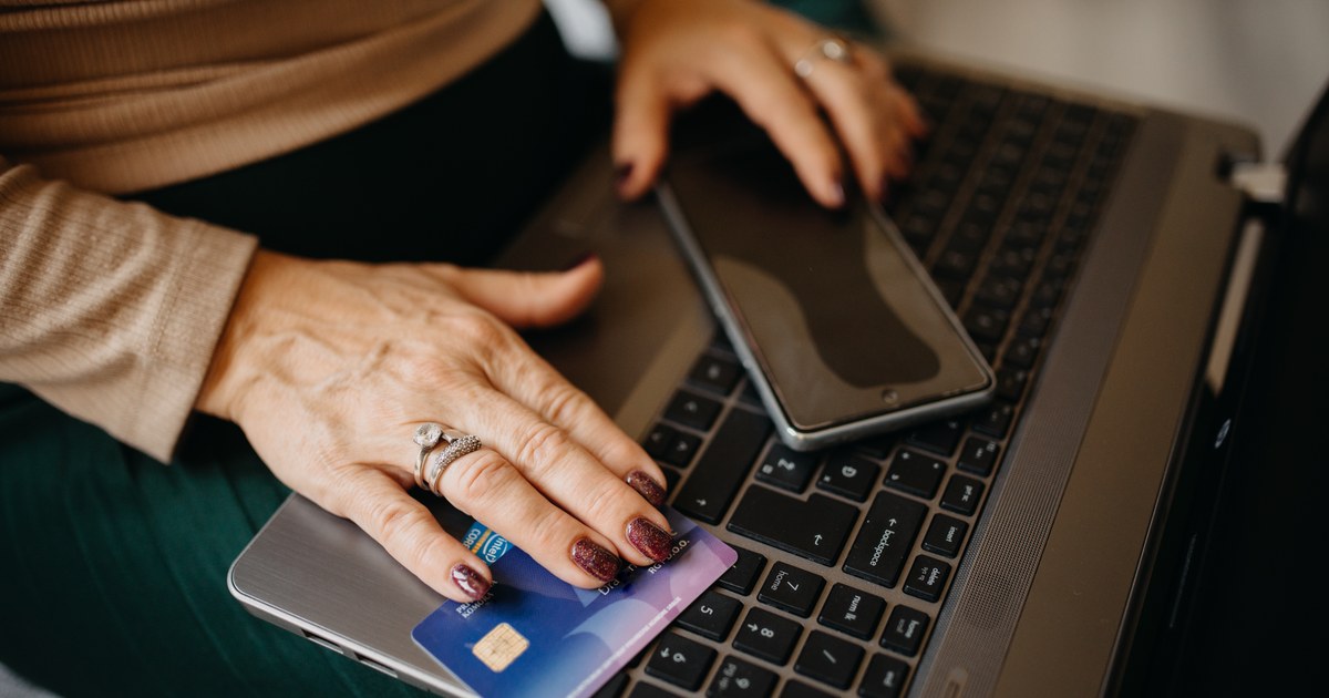 Person holding a payment card and smartphone while using a laptop at home