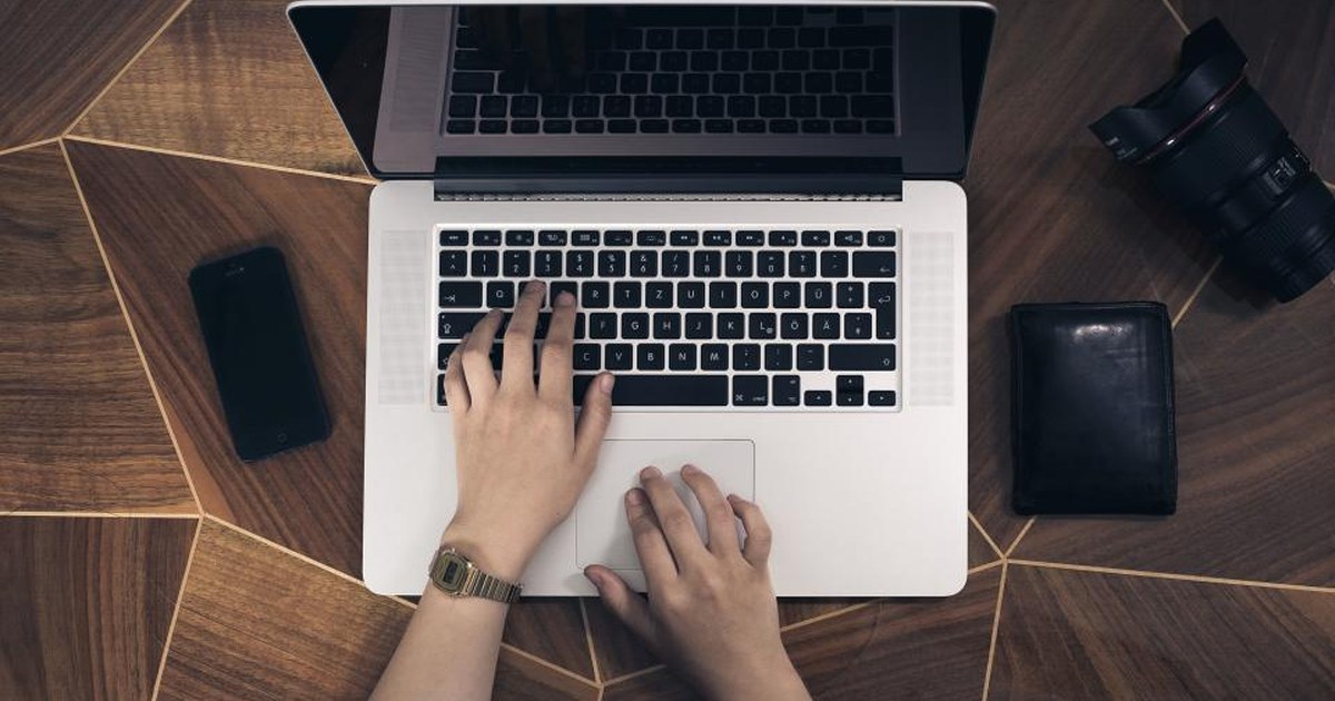 Person typing on a laptop at a desk with a smartphone and wallet nearby