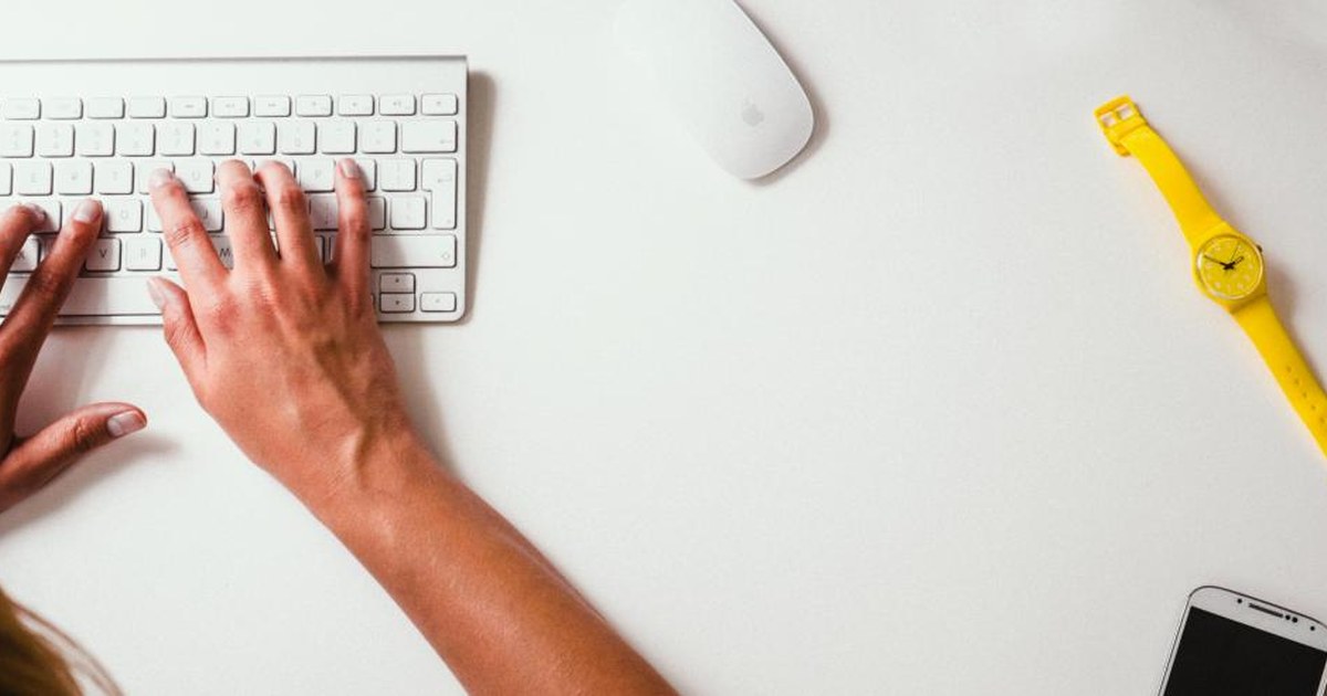 Person typing on a keyboard at a desk with a smartphone, illustrating online casino account and identity checks.