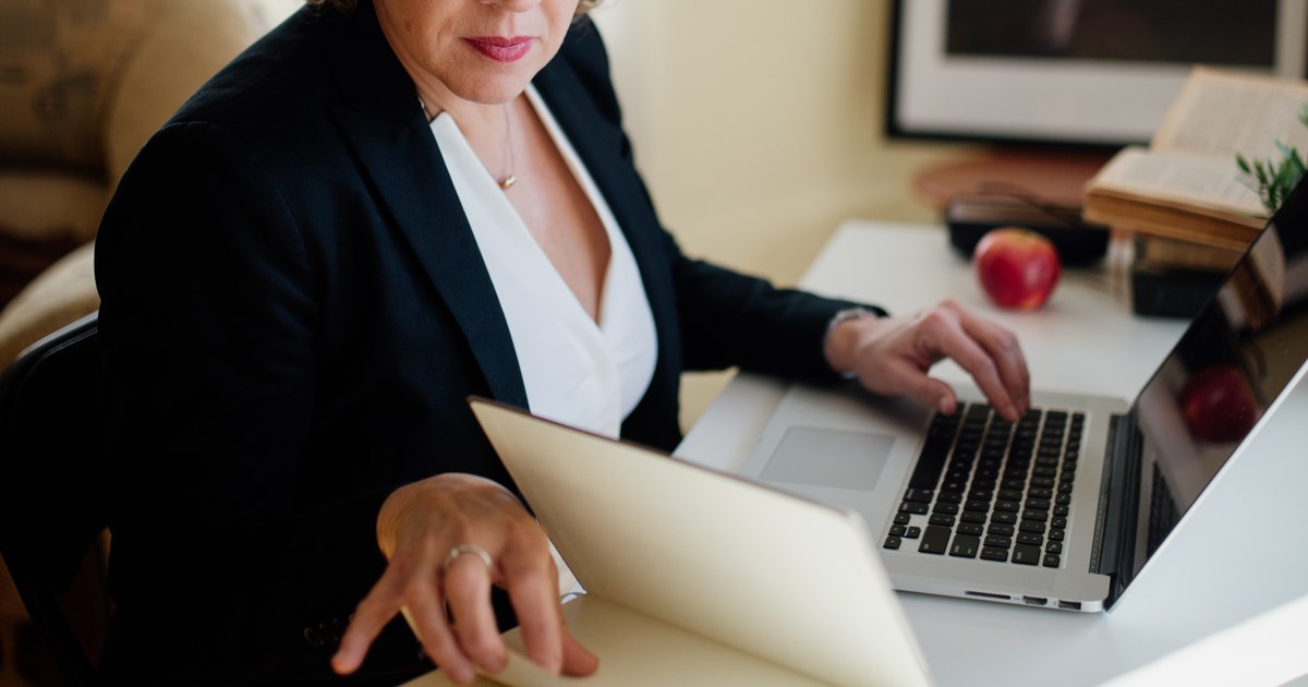 Person at a desk using a laptop and reviewing documents