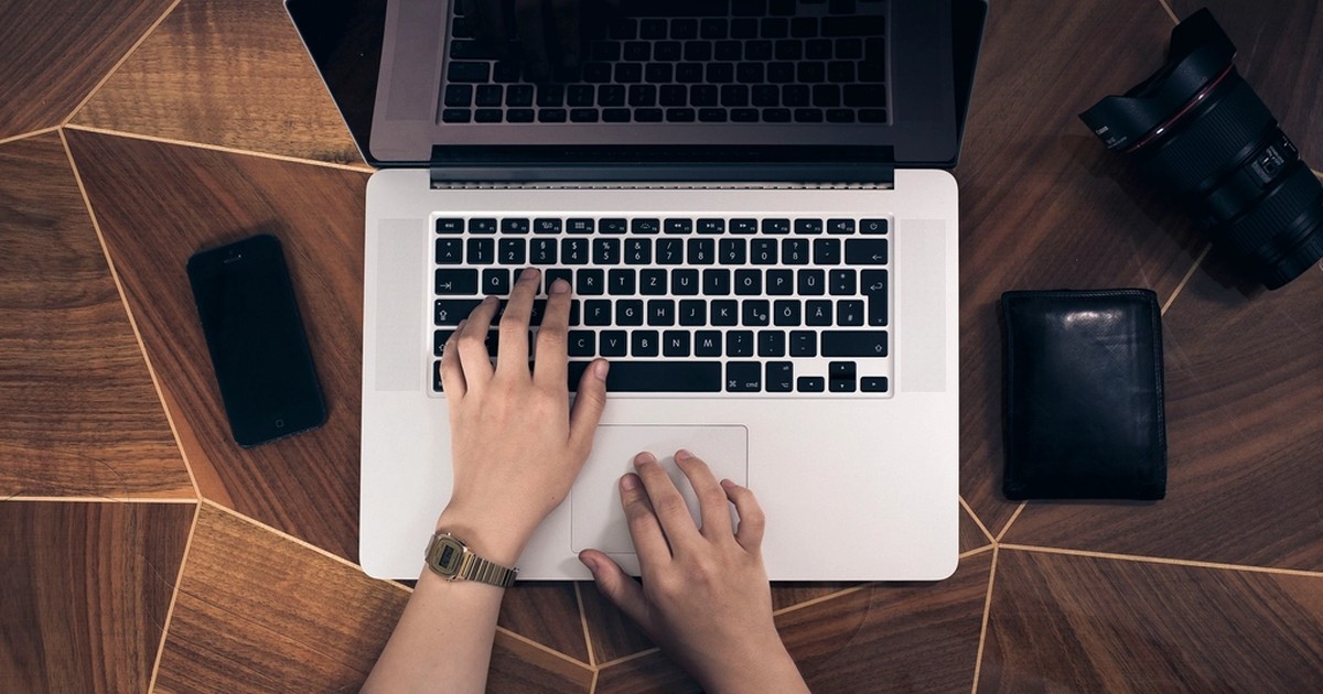 Person using a laptop with a smartphone and wallet on a desk