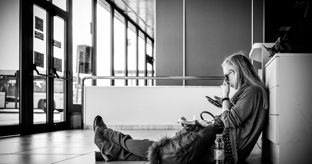 Adult person sitting in a station concourse in Rome, Italy, looking at a smartphone.