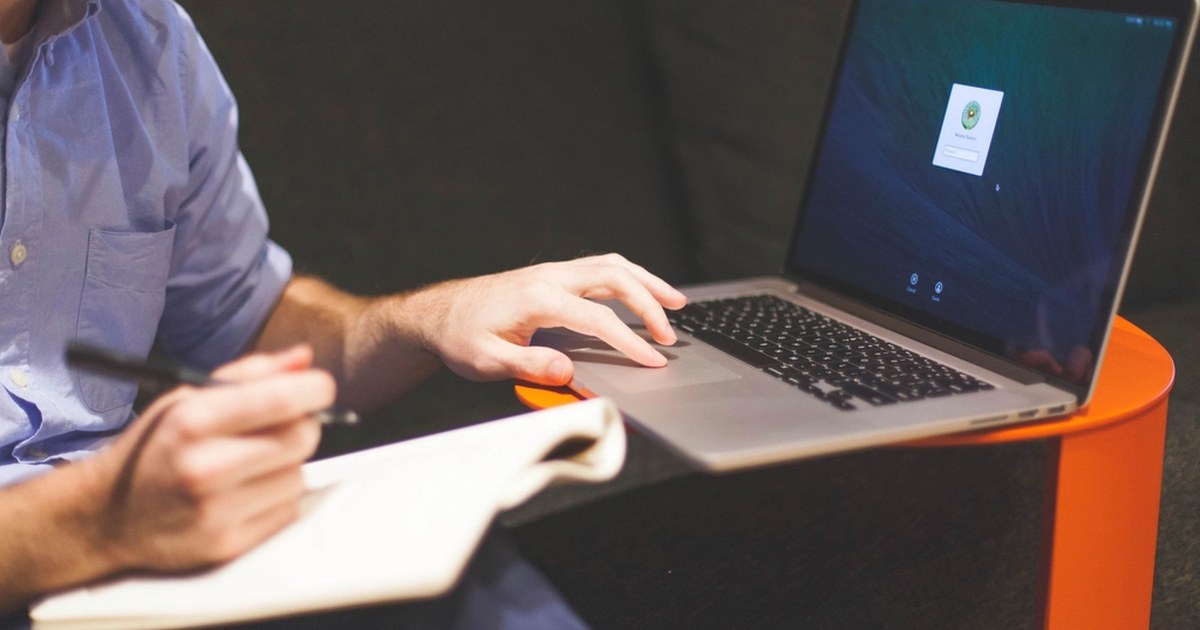 Person using a laptop and taking notes while managing an online account at a desk