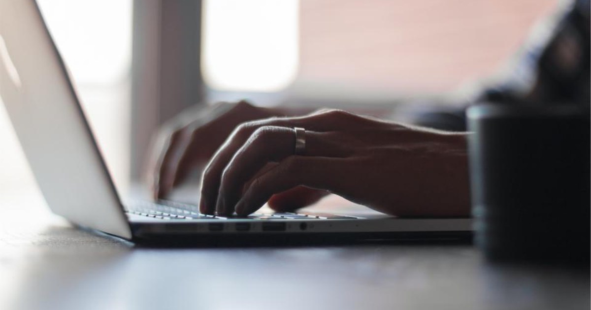 A person typing on a laptop keyboard at a desk in soft daylight