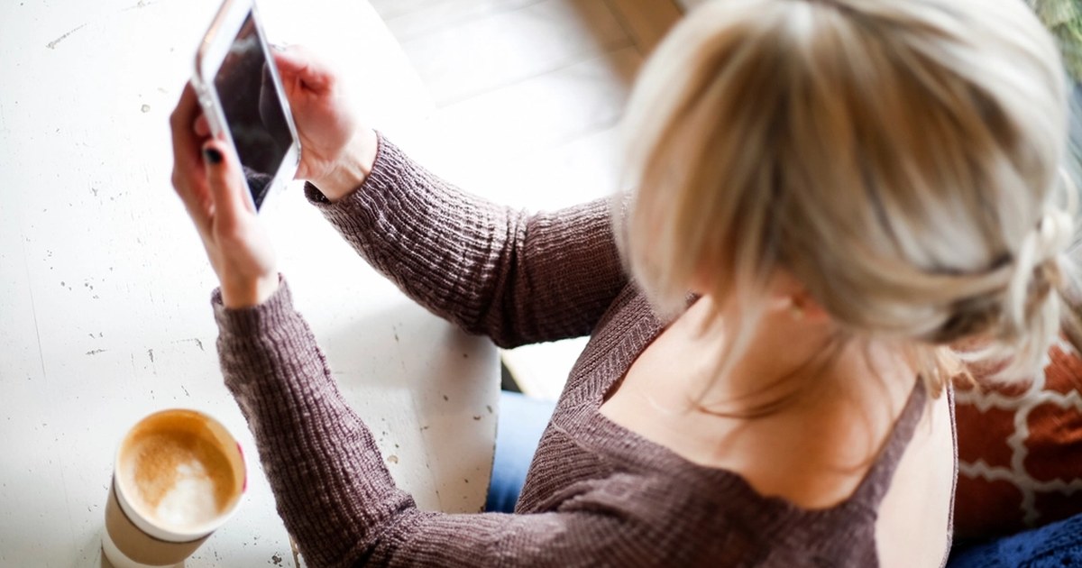 A person sitting at a table using a smartphone next to a coffee cup