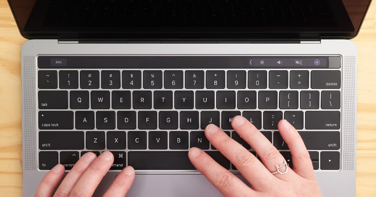 Close-up of a person typing on a laptop keyboard at a wooden desk