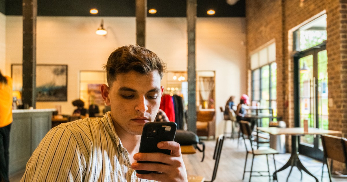 A man checking his smartphone in a cafe while reviewing an online casino account on his phone