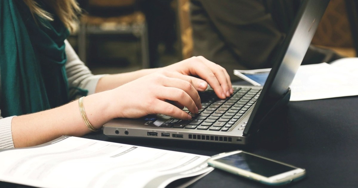Person typing on a laptop at a desk with a smartphone, representing online casino account management